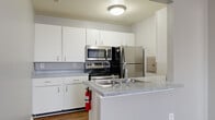 This single-floor residence offers a clean, functional layout designed for comfortable everyday living. The kitchen is equipped with stainless steel appliances, including an electric range, over-the-range microwave, and a French door refrigerator. White cabinetry provides ample storage, while speckled grey laminate countertops extend to a peninsula with a double stainless steel sink — ideal for meal prep and casual use. Wood-look flooring runs throughout the kitchen, adding warmth to the space.

The living area features vaulted ceilings, a ceiling fan, and large windows dressed with vertical blinds, allowing for generous natural light. Soft carpeting and neutral grey walls create a calm, versatile atmosphere throughout the living and bedroom spaces.

Multiple bedrooms offer well-sized footprints, each finished with plush carpet, grey walls, and windows with blinds to control light and privacy. The rooms provide a quiet, adaptable setting suitable for various configurations.

Two bathrooms serve the unit. One features a walk-in shower with a frosted glass door and wood-look flooring, while the second includes a full tub-shower combination, a single-sink vanity with a framed mirror, and matching wood-look flooring. Both bathrooms are finished in a consistent, understated style that complements the rest of the home.