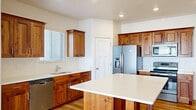 This two-floor home offers a thoughtfully designed layout with a clean, neutral aesthetic throughout. The kitchen serves as a functional centerpiece, showcasing rich wood cabinetry, a white quartz-topped island, stainless steel appliances including a French door refrigerator, built-in microwave, and range, as well as a stainless steel sink and dishwasher. Hardwood flooring runs through the kitchen and dining areas, adding warmth and continuity. The open living room features soft carpeting and a ceiling fan with lighting, creating a comfortable and well-ventilated space that flows seamlessly into the kitchen through an open archway. Natural light filters in through the kitchen window, brightening the space. A dedicated laundry room houses a full-size washer and dryer with overhead shelving for additional storage. The bathroom is clean and functional, equipped with a full-size soaking tub and shower combo. Bedrooms are carpeted and include generous closet space with classic paneled bifold doors. The entry level features tile flooring at the front door, with a staircase leading to the upper floor. Throughout the home, white craftsman-style interior doors and neutral walls provide a cohesive, move-in-ready finish.