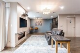 Located at 479 Valley St in Maplewood, NJ, this thoughtfully designed single-floor space combines modern aesthetics with functional living. Rich, dark hardwood flooring runs continuously throughout, anchoring the cohesive and contemporary interior.

The living area serves as the centerpiece of the space, featuring a sleek built-in linear fireplace paired with a wall-mounted television and a stylish pendant light fixture. A leather sofa, area rug, and track lighting create a warm and inviting atmosphere, while large windows with blinds allow natural light to fill the room and offer views of the surrounding neighborhood.

The kitchen is outfitted with dark espresso cabinetry extending to the ceiling, complemented by light gray countertops, a stainless steel refrigerator, an over-the-range microwave, and a single-basin sink — providing a clean, modern workspace with ample storage.

The dining area is a welcoming, intimate space featuring a round table with upholstered chairs, a wooden bench along the wall, and a lush potted plant that adds a natural touch against the neutral gray walls.

The floor plan also includes a versatile recreation area, visible in the dollhouse view, which accommodates a foosball table and additional seating, making this space well-suited for both relaxation and entertainment.