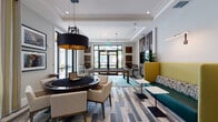 Located at 15616 SW 127th Ave in Miami, FL, this single-floor amenity clubhouse is thoughtfully designed to provide a refined yet welcoming environment for recreation and community engagement. The entrance lobby greets visitors with large-format marble-look porcelain tile flooring, curated botanical arrangements, and framed artwork that sets an upscale tone. Glass-paneled doors with decorative etched designs lead into a dedicated business center, where wood-look flooring and modern furnishings create a professional workspace. An elevator and well-lit corridors connect the various areas of the facility, with warm accent lighting and additional artwork lining the hallways. The centerpiece of the space is a vibrant game lounge featuring multi-toned wood plank flooring, a poker/game table with a bold industrial pendant light overhead, a billiards table, and a large wall-mounted television flanked by a tufted lounge seating area with yellow and teal upholstery. Floor-to-ceiling windows and glass doors flood the lounge with natural light and provide views to the outdoor pool area. Casual game stations, including oversized Connect Four and Jenga, add a playful touch throughout the transitional areas. The overall design balances contemporary aesthetics with comfort, making this clubhouse a well-appointed social and professional hub.