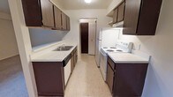 This single-floor, 1-bedroom, 1-bathroom unit is designed with functionality and practicality in mind. The galley-style kitchen is a standout feature, offering a well-organized, corridor layout with dark-toned cabinetry lining both walls from floor to ceiling. The kitchen is equipped with white appliances, including an electric range and a full-sized refrigerator, along with a double-basin sink and generous counter space on both sides. Additional open shelving provides extra storage options. Light-toned flooring runs through the kitchen, contributing to a clean and bright feel. A closet with louvered doors is conveniently accessible from the kitchen area, adding practical storage. The neutral wall tones throughout keep the space feeling open and easy to personalize. The overall layout is thoughtfully designed to maximize every square foot, making it a comfortable and efficient living space well-suited for individuals or couples seeking a manageable, low-maintenance home.