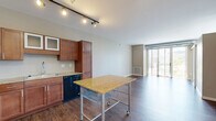 Located at 5250 Liberty Avenue in Pittsburgh's Bloomfield neighborhood, this one-bedroom, one-bathroom unit offers a well-designed layout with modern finishes throughout. The open-concept kitchen and living area serves as the heart of the home, featuring rich hardwood-style flooring, track lighting, and large floor-to-ceiling sliding glass doors that flood the space with natural light and provide outdoor views. The kitchen is well-appointed with warm-toned wood cabinetry, granite countertops, black appliances including a range, microwave, refrigerator, and dishwasher, plus a deep stainless steel sink. A frosted glass sliding barn door adds a contemporary architectural touch, separating the living area with style. Exposed ductwork along the ceiling lends an industrial character to the space. The living area is generously proportioned with ample room for furniture arrangements. The bedroom is carpeted for comfort, features a large window with natural light and outdoor views, and includes access to a walk-in closet. The bathroom is finished with hardwood-style flooring, a wood vanity with a white countertop, and a full soaking tub with shower. Four closets throughout the unit provide exceptional storage capacity for a space of this size.