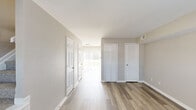 This two-story space is designed with a clean, functional aesthetic throughout. Consistent wood-look flooring runs across both levels, complemented by neutral greige wall tones and crisp white trim, creating a cohesive and understated interior palette. The open layout of the main level is highlighted by a corridor that connects the living area to additional rooms, with multiple white panel doors — including louvered closet doors — adding subtle architectural detail. Natural light filters in through windows fitted with horizontal blinds, brightening each room effectively.

The galley-style kitchen is a practical centerpiece, featuring warm honey-toned wood cabinetry on both sides, stone-look countertops, a stainless steel sink, and white appliances including a gas range and refrigerator. Upper and lower cabinets provide ample storage, while the wood-look flooring continues seamlessly into the space.

The bedrooms across both floors share a similar design language — neutral walls, wood-look flooring, and windows that allow natural light to enter. At least one bedroom includes a sliding closet with built-in rod storage. Textured ceilings appear in select rooms, adding subtle variation. Overall, the space presents a well-maintained, neutral canvas suitable for a variety of living arrangements.