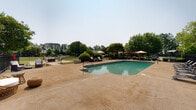 Located at 180 W Dublin Dr in Madison, Alabama, this outdoor amenity space is thoughtfully designed for both relaxation and social gathering. At its center is a generously sized swimming pool with a classic freeform shape, surrounded by a stamped concrete pool deck equipped with lounge chairs for sunbathing. The pool area is enclosed by a sleek black iron fence, providing security while maintaining open sightlines to the surrounding greenery.

Adjacent to the pool, a dedicated lounge area features a cushioned outdoor sofa and armchair arranged around a fire pit table, set on a brick-accented patio — an inviting spot for evening gatherings. Manicured landscaping with curved garden beds, flowering plants, and trimmed shrubs adds color and charm throughout the grounds.

A separate outdoor dining and grilling zone includes multiple picnic-style tables shaded by large market umbrellas, alongside stainless steel gas grills and a charcoal grill, making it well-suited for cookouts and communal meals. A covered pergola structure provides additional shaded seating nearby. The entire complex is framed by mature trees that offer a natural backdrop, enhancing the sense of privacy and tranquility within this well-appointed outdoor retreat.