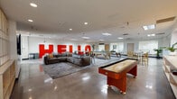 Located at 3910 Elati St in Denver, CO, this single-floor commercial space delivers a dynamic, modern workplace environment designed to balance productivity and recreation. The layout is anchored by a spacious open common area highlighted by a bold, oversized "HELLO" wall installation in red — a defining visual statement that sets the tone for the space's energetic character. Polished concrete floors run throughout, reflecting light and lending an industrial-modern aesthetic that ties all areas together cohesively.

The game and lounge area is a standout feature, offering a shuffleboard table, pool table, and ample seating including a large sectional sofa and accent chairs, all arranged to encourage informal gathering. An adjacent reception-style lounge features warm tan modular seating and direct sightlines into private glass-windowed offices. The kitchen and café zone is equipped with a long counter bar lined with orange stools, pendant lighting, and a sink — ideal for breaks and informal collaboration.

A dedicated dining nook features booth-style seating set against a textured accent wall with pendant lighting, providing a more intimate setting. Throughout the space, open high-top tables, wood-slatted partitions, open shelving with curated items, and abundant indoor greenery contribute to a welcoming, contemporary office atmosphere.