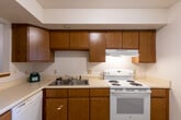 This single-floor residence offers a practical and well-organized layout. The kitchen is equipped with warm oak cabinetry extending to the upper walls, providing ample storage. White appliances include a full-size refrigerator, electric coil range with an overhead exhaust hood, and a dishwasher. Light wood-look flooring runs throughout the kitchen, complementing the neutral countertops and double-basin sink.

The hallway connects the main areas and features a full-size closet with solid wood doors and overhead ventilation. Carpeted bedrooms offer a comfortable feel underfoot, with one room featuring a ceiling fan with integrated lighting, a wall pass-through detail, and a double-door closet. Windows fitted with horizontal blinds allow natural light into the bedrooms.

The bathroom area is notably well-appointed, featuring dual vanities with oak cabinetry, light countertops, mirrored medicine cabinets, and overhead vanity lighting. Tile flooring in the bathroom transitions smoothly to the surrounding carpeted areas. Throughout the unit, textured ceilings, neutral wall tones, and consistent warm wood trim details create a cohesive, understated aesthetic.