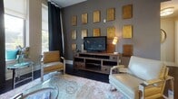 Located in the heart of Richmond, Virginia, this single-floor residence at 200 N Third St offers a well-appointed interior defined by modern design and quality finishes. The living area makes a strong impression with its deep charcoal accent wall, dark hardwood flooring, and generous natural light filtering through large windows dressed with floor-length drapes. The space is anchored by a rustic media console and complemented by eclectic décor details that add character and warmth.

The kitchen is a standout, featuring stainless steel appliances including a full-size refrigerator, range, and dishwasher. Two-tone cabinetry pairs crisp white uppers with dark lower cabinets, set against a metallic tile backsplash and light countertops. Pendant lighting and recessed fixtures provide both function and ambiance.

The bedroom offers a serene retreat with vaulted ceilings, neutral tones, and a walk-in closet accessible through a clean white doorframe. A second bedroom provides ample space with a dedicated work area by the window and views of the surrounding greenery.

The bathroom is finished with large-format white wall tiles, dark mosaic floor tiles, and a decorative multicolored mosaic accent strip in the walk-in shower, adding a refined artistic touch. Throughout the residence, the cohesive design palette and quality materials create a polished, comfortable living environment.
