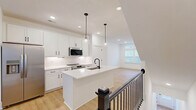 Located at 2701 Rozzelles Ferry Rd in Charlotte, NC, this contemporary 3-story home offers a well-designed layout across three distinct levels. The ground floor houses a spacious attached garage with drywall-finished walls, a dedicated utility area with a water heater, and staircase access to the upper levels. The main living floor is the heart of the home, featuring an open-concept kitchen, dining, and living area filled with natural light. The kitchen is appointed with crisp white shaker cabinetry, quartz countertops, a large center island with an undermount sink and matte black faucet, stainless steel appliances, a subway tile backsplash, and elegant glass pendant lighting. Light-toned hardwood-style flooring flows throughout this level, complementing the bright, neutral palette. A balcony provides outdoor access directly from the main floor. The upper floor is home to two well-proportioned bedrooms, each featuring ceiling fans, recessed lighting, and generous natural light from multiple windows. The primary bedroom includes dedicated closet space and a private en-suite bathroom. The bathrooms throughout are finished with marble-style tile, white vanities, quartz countertops, and distinctive matte black fixtures and hardware, including a glass-enclosed shower. A dedicated laundry area and ample closet storage complete this thoughtfully designed home.