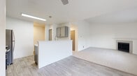 Located at 1221 Mottman Rd SW in Tumwater, Washington, this single-floor unit offers a clean, modern aesthetic throughout its well-designed layout. The open-concept kitchen is a functional highlight, featuring gray shaker-style cabinetry, a white subway tile backsplash, a breakfast bar peninsula, and a full suite of stainless steel appliances including a Whirlpool electric range, over-the-range microwave, and a full-size refrigerator. Light wood-look flooring flows through the kitchen and main living areas, transitioning seamlessly to plush carpet in the living room and bedrooms. The spacious living room is anchored by a fireplace with a clean white mantle and opens to an area with sliding glass door access and a ceiling fan overhead. Large windows throughout invite natural light and outdoor views of the surrounding greenery. The bedrooms offer comfortable proportions, each with closet storage and baseboard heating. The bathrooms are finished with clean white tub/shower surrounds, and one features wood-look flooring with a gray vanity and brushed gold hardware. A hallway with wood-look tile connects the main spaces, with additional closet access and well-defined room separation throughout.