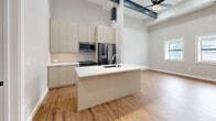 Located at 1100 Washington Ave in Golden, CO, this modern single-floor residence offers three bedrooms, two bathrooms, and a thoughtfully designed open-concept layout. The kitchen and living area form the heart of the home, showcasing soaring ceilings with striking exposed steel beams and a ceiling fan that enhances the airy, loft-inspired ambiance. The kitchen is outfitted with flat-front cabinetry in a warm greige tone, stainless steel appliances, a subway tile backsplash, and a central island with a white countertop and integrated sink — ideal for both cooking and casual dining. Light oak hardwood flooring runs throughout the main living areas, complementing the neutral palette. Hallways connect the bedrooms with clean lines and recessed lighting overhead. The three bedrooms feature plush carpeting and are accented by modern gray panel doors with matte black hardware. Each bedroom includes dedicated closet space. The two bathrooms are finished with large-format gray tile flooring, floating vanities with white countertops, and glass-enclosed walk-in showers clad in vertical gray tile. A dedicated laundry area adds everyday convenience. The overall design aesthetic is clean, contemporary, and cohesive throughout.