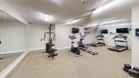 Located at 59 Concession St in Cambridge, Ontario, this fitness room offers a practical and well-organized space dedicated to exercise and wellness. The room is finished with neutral white walls, durable carpet flooring, and bright fluorescent overhead lighting that ensures excellent visibility throughout.

The cardio section is a standout feature, housing two treadmills and an elliptical trainer, each positioned conveniently beneath wall-mounted flat-screen televisions — allowing users to stay entertained during their workouts. A stationary bike further rounds out the cardio options available.

The strength training area is thoughtfully equipped with a multi-function cable machine, a weight bench with barbell rack, and an assortment of dumbbells, barbells, and weight plates. A large wall-to-ceiling mirror is installed along one side, helping users monitor their form and adding a sense of additional depth to the space.

A wall-mounted sanitizing station and clearly posted workout guidelines reflect a commitment to cleanliness and user awareness. A fire extinguisher and visible safety signage further ensure the space meets safety standards. The room's compact yet functional layout makes efficient use of the available floor area, providing a comprehensive workout experience suitable for a variety of fitness goals and routines.