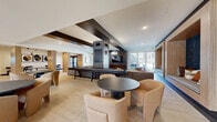 Located at 10631 Parallel Pkwy in Kansas City, KS, this expansive single-floor communal space offers a thoughtfully designed interior spanning a generous footprint. The layout is organized into distinct functional zones while maintaining an open, cohesive flow throughout.

The kitchen area is a standout feature, outfitted with warm wood cabinetry, dark countertops, a hexagonal tile floor, and stainless steel appliances. Floor-to-ceiling windows flood the space with natural light and provide exterior views, while open shelving and ample counter space make it well-suited for events and gatherings.

The living and lounge areas showcase contemporary design elements, including light hardwood flooring, recessed lighting, and exposed dark ceiling beams. A dramatic floor-to-ceiling tiled fireplace serves as a central focal point, flanked by glass doors that open to an outdoor area. A built-in lounge nook with textured wallcovering and plush sectional seating provides an intimate retreat within the larger space.

The entry area features soaring double-height ceilings, geometric hexagonal tile flooring, sculptural pendant lighting, and an elevated mezzanine-style architectural element. Additional seating nooks with warm wood-framed surrounds offer semi-private gathering options. Throughout, the design balances modern industrial aesthetics with warm, natural materials.
