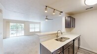 Located at 285 Reed Rd in Beavercreek, Ohio, this one-bedroom, one-bathroom residence offers a well-designed layout that maximizes its comfortable footprint. The open-concept main area seamlessly connects the kitchen and living room, creating a bright, cohesive space. The kitchen is outfitted with dark espresso cabinetry, light quartz countertops, a peninsula with a double stainless steel sink, stainless steel appliances including a refrigerator, range, and microwave, and wood-look flooring. Track lighting adds a modern touch overhead. The living area features plush carpeting, a ceiling fan, and abundant natural light from large windows and a sliding glass door that opens to a private balcony with outdoor views. Carpeted stairs with a warm wood handrail lead between levels. The bedroom is a well-proportioned, quiet retreat with soft carpet and a sliding door to an additional outdoor space. The bathroom includes a dark vanity with quartz countertop, a tiled soaking tub and shower combination, and wood-look flooring. A dedicated laundry room houses a full-size washer and dryer alongside built-in shelving, offering excellent storage and everyday convenience throughout the home.