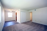 Located at 3605 Kecoughtan Rd in Hampton, Virginia, this single-floor residence offers a straightforward and functional layout designed for comfortable everyday living. The living area greets you upon entry through a white exterior door, featuring warm neutral-toned carpet and clean white walls that create a bright, open atmosphere. Natural light filters in through blinded windows, adding a welcoming feel to the space. The kitchen is well-equipped with warm oak cabinetry — both upper and lower — complemented by granite-style laminate countertops and a double stainless steel sink. A white electric range, under-cabinet ventilation hood, and a full-size white refrigerator complete the kitchen's practical setup. Tile flooring runs throughout the kitchen, providing easy maintenance. The bedrooms are carpeted and generously sized, with neutral walls and windows that allow ample natural light. One bedroom features a closet with sliding doors and a ceiling fan fixture, while another includes a reach-in closet with a hanging rod for convenient storage. The bathroom is clean and functional, appointed with a full tub-shower combo surrounded by white subway tile, and standard fixtures throughout. The overall ambiance of the home is clean, neutral, and move-in ready.