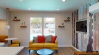 Located at 2376 Fairfield Ave in Fairfield, California, this single-floor community clubhouse is a well-appointed gathering space designed with a modern, eclectic aesthetic. The interior is unified by warm hardwood-style flooring, recessed lighting, and a distinctive teal-painted ceiling that adds a pop of color and visual interest throughout.

The lounge area serves as the social centerpiece, featuring large windows that frame views of an outdoor pool and seating area, flooding the space with natural light. A bold, textured accent wall with a distressed, multicolor mural adds an artistic focal point, complemented by a wall-mounted flat-screen television and floating wood shelves for decorative display.

Adjacent to the lounge is a functional kitchenette area highlighted by a white quartz-topped island with industrial-style bar stools, ideal for casual dining or socializing. A striking navy blue hexagonal tile backsplash frames the countertop wet bar area, while a mid-century modern brass chandelier with globe pendants provides warm, ambient lighting overhead. Decorative round mirrors and open shelving complete the contemporary look.

The space also includes a foosball table, offering a fun recreational element for residents. A direct exterior door provides easy access to the outdoor areas. Overall, this clubhouse strikes a balance between stylish design and practical amenity, making it an inviting hub for community gatherings.