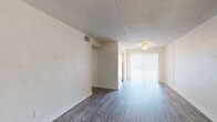 This single-floor residence offers a clean, functional layout designed for comfortable everyday living. Throughout the home, durable wood-look plank flooring in a cool gray tone provides a cohesive and low-maintenance foundation, complemented by crisp white walls and textured ceilings.

The main living area is open and generously proportioned, offering ample space for furnishing and personalization. A sliding glass door fitted with vertical blinds fills the area with natural light while providing access to the outdoors. The entry area features a solid front door with a sidelight window, creating a welcoming transition into the home.

The kitchen is well-equipped with white shaker-style cabinetry, light granite-look countertops, a stainless steel double-basin sink, and black appliances including an electric range and a full-size refrigerator. A window above the sink adds natural light to the workspace.

The bedrooms are quietly situated within the floor plan, each featuring wood-look flooring, neutral walls, and vertical blind-covered windows that allow for natural light and privacy. One bedroom benefits from two windows, enhancing its bright, airy feel.

The bathroom is neatly finished with a white vanity, light countertop, a tiled tub-shower combination with chrome fixtures, and matching wood-look flooring that carries through from the rest of the home. The overall ambiance is clean, neutral, and move-in ready.
