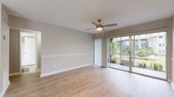 This single-floor residence offers a thoughtfully designed layout that balances comfort and functionality throughout. The open living area is finished with light wood-tone flooring and neutral gray walls accented by a classic chair rail, creating a clean and cohesive aesthetic. A ceiling fan with a built-in light fixture keeps the space comfortable, while large sliding glass doors flood the room with natural light and provide direct access to an outdoor area framed by lush tropical greenery. The dedicated dining area features a stylish chandelier and flows seamlessly into the kitchen, which is equipped with white shaker-style cabinetry, light stone countertops, stainless steel appliances including a dishwasher and range, and a striking mosaic tile backsplash that adds a contemporary touch. A pass-through opening connects the kitchen to the dining space, enhancing the open feel. The bedroom is generously sized with soft carpeting, a window allowing natural light, and direct access to a walk-in closet. The bathroom is clean and functional, featuring a full tub-shower combo with white tile surround and brushed nickel fixtures. A textured ceiling is present throughout, adding subtle architectural character to every room.