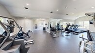 Located at 1710 Devonshire Rd in Hauppauge, NY, this fitness center offers a thoughtfully designed, single-floor layout built to support a full range of exercise activities. The main exercise room is generously proportioned, featuring durable rubber flooring, recessed lighting, and vaulted ceilings in select areas that lend an open, airy feel to the space. Large windows along multiple walls allow abundant natural light to filter in, creating a bright and energizing environment. Full-length mirrors are strategically positioned to maximize the sense of space and assist users during workouts. The room is outfitted with a diverse array of equipment, including treadmills, elliptical machines, stationary bikes, cable weight machines, a dumbbell rack, and a rowing machine, providing options for both cardio and strength training. A wall-mounted TV adds convenience for entertainment during workouts. The facility also includes a dedicated entrance with glass double doors opening to the outdoors, ensuring easy access. A clean, ADA-accessible bathroom with tile flooring, a marble-top vanity, a lighted mirror, and grab bars rounds out the space, ensuring both comfort and accessibility for all users.