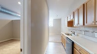 This single-floor unit offers a practical and well-organized layout designed for comfortable everyday living. The kitchen is a standout feature, equipped with warm honey-toned wood cabinetry, light countertops, a tiled backsplash, and a full suite of black appliances including an electric range, over-the-range microwave, dishwasher, and a stainless steel refrigerator. Light wood-style vinyl flooring runs throughout the kitchen and hallway, creating a clean and cohesive aesthetic. The open living area is generously sized with soft wall-to-wall carpeting underfoot and recessed lighting overhead, offering a bright and welcoming atmosphere. A window along one wall allows natural light to filter in, enhancing the sense of openness. A secondary carpeted room, accessed from the main living space, features exposed HVAC ductwork along the ceiling — an industrial design element that adds visual character. The bathroom is finished with the same light wood-style flooring and includes a vanity with wood cabinetry, a toilet, and a full bathtub and shower combination. Neutral, warm-toned walls throughout the unit provide a versatile backdrop suitable for a variety of interior styles.