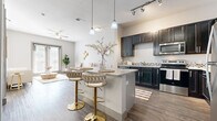 This single-floor residence is designed with a contemporary open-concept layout that seamlessly connects the kitchen, dining, and living areas. The kitchen is a standout feature, equipped with dark charcoal cabinetry, granite countertops, mosaic tile backsplash, and a full suite of stainless steel appliances including a refrigerator, range, microwave, and dishwasher. A central island with pendant lighting overhead provides additional prep space and casual seating with bar-height stools. Wood-look flooring extends throughout the main living areas, adding warmth and continuity to the space.

The living room is generously sized, anchored by large sliding glass doors that invite natural light and offer outdoor views. A ceiling fan enhances comfort in this bright, airy area. The bedroom features plush carpeting, multiple windows for natural light, and access to a spacious walk-in closet outfitted with wire shelving systems for organized storage.

A tiled hallway connects the private areas of the home, leading to the bathroom and closet spaces. Neutral gray tones, modern hardware, and tasteful design details give the entire residence a cohesive, polished aesthetic throughout.