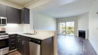 Located at 7077 Alvern St in Los Angeles, CA, this one-bedroom, one-bathroom residence offers a well-designed single-floor layout that makes efficient use of its space. The open-concept living and kitchen area serves as the heart of the unit, where rich hardwood-style flooring flows throughout. The kitchen features dark espresso cabinetry, a white quartz peninsula countertop, and a full suite of stainless steel appliances including a refrigerator, range, microwave, and dishwasher. A breakfast bar provides additional functionality and separation between the kitchen and living areas. The living room is bright and inviting, highlighted by a classic fireplace and sliding glass doors that open to a private balcony with lush outdoor views, allowing natural light to fill the space. The bedroom offers plush carpeting, a generous footprint, and a window overlooking greenery, creating a calm and comfortable retreat. A dedicated closet provides ample storage. The bathroom is clean and modern, featuring dark vanity cabinetry, a white countertop with an undermount sink, a mirror, and a shower-tub combination. Neutral wall tones throughout lend a versatile, move-in-ready feel to this well-appointed Los Angeles residence.
