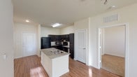 This single-floor residence offers a well-organized layout connecting living, kitchen, and bedroom spaces in a cohesive flow. The open-concept kitchen serves as a central hub, featuring dark espresso cabinetry paired with light granite countertops, a suite of black appliances including a refrigerator, range, and microwave, and a white kitchen island with a built-in sink. Wood-style flooring runs throughout the main living and kitchen areas, complemented by track lighting overhead.

The living area extends from the kitchen with ample room to accommodate furnishings, and benefits from natural light entering through multiple windows fitted with blinds. Ceiling fans with integrated lighting fixtures are present in the bedrooms, which are carpeted for added comfort. One bedroom features several windows on two walls, allowing for generous natural light and exterior views.

Two bathrooms serve the unit. One includes dark vanity cabinetry, a single-sink vanity with a large mirror, and a bathtub with a shower rod. The second bathroom is outfitted with accessibility features, including multiple grab bars positioned around the bathtub and toilet areas, along with wood-style flooring. Neutral, light-toned walls throughout the unit contribute to a clean and cohesive aesthetic.