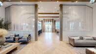Located at 7100 Summerside Dr in Whitsett, NC, this thoughtfully designed single-floor community space blends modern farmhouse aesthetics with upscale finishes throughout. The open-concept layout is anchored by striking light-toned herringbone hardwood floors that flow seamlessly from one zone to the next, creating a cohesive and inviting atmosphere.

Soaring ceilings with exposed wood beams add architectural warmth and volume, while sheer floor-to-ceiling drapery panels flank structural columns at the entrance, framing the space with an elegant, airy quality. Natural light pours in through oversized windows and glass French doors, enhancing the bright and welcoming ambiance.

The living area features multiple distinct seating arrangements, including a cozy lounge anchored by a floor-to-ceiling whitewashed brick fireplace topped with a mounted television and flanked by framed artwork. An arched ceiling detail overhead adds dramatic architectural interest. A separate sitting area showcases a sculptural 3D wall treatment, paired with eclectic furnishings and a statement chandelier.

The kitchen bar area is outfitted with a marble-topped island, black Windsor barstools, lantern pendant lighting, and exposed brick accent walls. A full-height black refrigerator and glass-paneled French doors leading to an outdoor area complete the functional yet stylish kitchen zone. The space as a whole conveys a refined yet relaxed character, ideal for community gathering and social interaction.