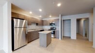 This single-story home offers a well-designed layout with three bedrooms and two full bathrooms. The kitchen serves as a central highlight, featuring dark wood-grain cabinetry extending to the ceiling, light granite countertops, and a full suite of stainless steel appliances including a refrigerator, gas range, microwave, and dishwasher. A central island with a matching granite surface provides additional workspace and casual seating. Recessed lighting illuminates the kitchen, which connects openly to the main living area. Light-toned tile flooring runs throughout the kitchen and common spaces, while the bedrooms are finished with plush carpeting. A dedicated utility/laundry room includes wire shelving and appliance hookups. The hallway connects the bedrooms efficiently, with two full bathrooms featuring matching wood-grain vanities, granite countertops, and tile flooring. One bathroom includes a full soaking tub with shower, while the second offers a streamlined layout. The bedrooms are generously proportioned, with ceiling fans, natural light from windows, and neutral wall tones creating a calm, comfortable atmosphere throughout.