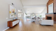This single-story community clubhouse is designed with an open, airy aesthetic that prioritizes natural light and spacious flow. The grand main lounge anchors the space with soaring vaulted ceilings, exposed beams, and expansive windows fitted with transom panels that flood the room with sunlight. Light hardwood floors run throughout, complementing the clean white walls and contemporary furnishings arranged on layered area rugs. Large glass entry doors open directly to the outdoors, enhancing the seamless indoor-outdoor connection.

A dedicated bar-height seating area features a long white counter with upholstered stools positioned before a generous wall of grid-pane windows overlooking an outdoor pool and landscaped surroundings. Adjacent to this is a bright lounge nook with modern white sofas framed by lush indoor plants and expansive garden views.

The conference room offers a vaulted ceiling, recessed lighting, and grid windows, accommodating a full boardroom table surrounded by ergonomic seating. A business center with glass-panel doors provides a professional workspace. The compact kitchenette includes streamlined cabinetry, open shelving, a coffee bar setup, and a stainless steel refrigerator — a practical amenity completing this well-appointed community facility.