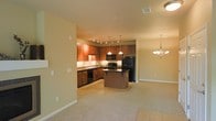 This single-floor residence offers an open-concept layout that seamlessly connects the kitchen, dining, and living areas, creating a spacious and functional environment. The kitchen is a standout feature, showcasing rich, warm-toned cabinetry with ample storage, granite countertops, and a full suite of black appliances, including a refrigerator, gas range, built-in microwave, and dishwasher. A central kitchen island provides additional prep space and serves as a natural gathering point. Track lighting above the kitchen, complemented by elegant pendant lights over the island, ensures the workspace is well-lit and visually appealing. The adjacent dining area is highlighted by a classic chandelier, adding a touch of sophistication to the space. Soft, neutral-toned carpeting flows through the living and dining areas, contributing to a warm and inviting ambiance, while tile flooring defines the kitchen zone. The walls feature a light, neutral palette that enhances the sense of openness and allows natural light to brighten the interior. The thoughtful layout and cohesive design elements make this a comfortable and practical single-level living space.