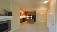 This single-floor residence offers an open-concept layout that seamlessly connects the kitchen, dining, and living areas, creating a spacious and functional environment. The kitchen is a standout feature, showcasing rich, warm-toned cabinetry with ample storage, granite countertops, and a full suite of black appliances, including a refrigerator, gas range, built-in microwave, and dishwasher. A central kitchen island provides additional prep space and serves as a natural gathering point. Track lighting above the kitchen, complemented by elegant pendant lights over the island, ensures the workspace is well-lit and visually appealing. The adjacent dining area is highlighted by a classic chandelier, adding a touch of sophistication to the space. Soft, neutral-toned carpeting flows through the living and dining areas, contributing to a warm and inviting ambiance, while tile flooring defines the kitchen zone. The walls feature a light, neutral palette that enhances the sense of openness and allows natural light to brighten the interior. The thoughtful layout and cohesive design elements make this a comfortable and practical single-level living space.