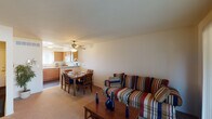 This three-floor residence offers a practical and comfortable layout across its levels, connected by a central staircase visible in the architectural overview. The main living area is carpeted and open in design, seamlessly integrating the living room, dining space, and kitchen. The living room features sliding glass doors that open to an outdoor balcony, allowing natural light to fill the space. A ceiling fan overhead adds functionality to the dining area, which sits adjacent to the kitchen. The kitchen is equipped with warm wood cabinetry, light countertops, a double sink, and white appliances including a range and built-in microwave, with a window providing natural light.

The bedrooms are carpeted and well-lit, each featuring multiple windows that bring in outdoor views and natural light, creating bright and airy spaces. A full bathroom includes a combined tub and shower, a white vanity with dual sinks, and tile flooring.

An additional flexible room with carpet and windows offers potential as a home office or sitting area. The lower level includes an unfinished basement with painted concrete walls, exposed wooden ceiling joists, and utility infrastructure, providing practical storage or conversion potential.