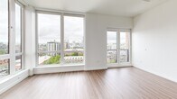 Located on the 14th floor at 535 NW 11th Ave in Portland's vibrant Pearl District, this one-bedroom, one-bathroom unit offers a thoughtfully designed open-concept layout with modern finishes and impressive city views. The combined kitchen and living area is anchored by expansive floor-to-ceiling windows that flood the space with natural light and frame sweeping panoramic views of the Portland skyline. A private balcony extends the living area outdoors, enhancing the sense of openness. The living area features smooth hardwood-style flooring that flows seamlessly throughout the main space. The kitchen is well-appointed with a clean two-tone cabinetry design—pairing white upper cabinets with warm wood-grain lower cabinets—complemented by light quartz countertops and a full suite of stainless steel appliances, including a French door refrigerator, range, dishwasher, and built-in microwave. The bedroom is carpeted and filled with natural light from a large window, offering a quiet retreat from the main living area. A dedicated closet provides organized storage. The bathroom features a full soaking tub and shower combination with clean white tile surround and polished chrome fixtures, maintaining the unit's crisp, contemporary aesthetic throughout.