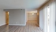 This single-story Spanish Mission property offers a practical and well-organized layout with a cohesive neutral color palette throughout. The open living and dining areas are finished with light wood-look luxury vinyl plank flooring that extends through much of the unit, creating a clean and consistent aesthetic. The dining area is accented by a classic chandelier, adding a subtle decorative touch, while vertical blinds along a sliding door provide light control and privacy. A dedicated living area features the same flooring with taupe-toned walls and textured ceilings, lending a warm, understated character to the space.

The kitchen is equipped with white cabinetry offering generous storage, light countertops, a built-in sink, a black electric range with overhead ventilation, and a dishwasher. The bedroom is carpeted with a ceiling fan and light fixture, providing comfort underfoot and efficient air circulation. Two full bathrooms each include a tub-shower combination with white tile surrounds. One bathroom features a large vanity mirror with a three-bulb light fixture, a white countertop, and undercabinet storage. Both bathrooms maintain a clean, functional design consistent with the overall tone of the space.