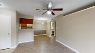 This one-bedroom, two-bathroom unit at 3003 Windchase Blvd in Houston, Texas offers a practical and comfortable single-floor layout. The open living room is highlighted by wood-style laminate flooring, a ceiling fan with light kit, a textured ceiling, and a classic wood-framed fireplace with a black surround — serving as a natural focal point. A sliding glass door leads to a private patio, filling the space with natural light and outdoor views. The kitchen is efficiently designed with warm wood cabinetry, granite-look countertops, white appliances including a range and refrigerator, and a breakfast bar that connects to the living area. The bedroom features plush carpeting, a ceiling fan, a window with outdoor views, and direct access to a closet. Both bathrooms are clean and functional: one includes a tub/shower combo with tiled surround, while the other features an extended vanity with a granite-look countertop, white cabinetry, and a large mirror. Neutral beige tones throughout the unit create a warm, cohesive ambiance. The layout is thoughtfully arranged to maximize usability across the compact but well-organized floor plan.