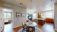 This single-floor residence showcases a thoughtfully designed open-concept layout that seamlessly connects the kitchen, dining, and living areas. The kitchen is a standout feature, equipped with stainless steel appliances, dual-tone cabinetry combining warm walnut and crisp white uppers, quartz countertops, a subway tile backsplash, under-cabinet lighting, and a central island with bar seating. Pendant lights and recessed fixtures provide layered illumination throughout.

The dining area accommodates a round table beneath a statement pendant light, while the adjacent living room offers generous space anchored by wood-look flooring, a ceiling fan, and sliding glass doors leading to a balcony. Multiple windows flood the space with natural light and offer outdoor views of surrounding greenery.

Both bedrooms are comfortably sized, each featuring ceiling fans, wood-look flooring, and windows with outdoor views. The neutral-toned walls lend a calm, restful atmosphere to each room. Two bathrooms serve the residence; one features a warm wood vanity with quartz countertops and a large mirror, while the second is a compact, efficiently designed space with coordinating finishes. Consistent warm wood flooring and neutral walls create a cohesive, modern aesthetic throughout.