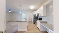 Located at 485 Crafton Cir in Charlottesville, VA, this single-level, one-bedroom, one-bathroom residence offers a well-designed layout that maximizes functionality and comfort. The open-concept living and kitchen area is the heart of the home, anchored by a large central island with granite countertops and a built-in sink, illuminated by stylish pendant lighting. White shaker cabinetry, a subway tile backsplash, and a full suite of stainless steel appliances — including a refrigerator, range, and microwave — complete the modern kitchen. Light wood-tone flooring flows throughout the main living areas, creating a warm and cohesive aesthetic. The living room features plush carpeting and a glazed entry door with a transom window above, inviting in natural light. The spacious bedroom is carpeted for comfort and includes a ceiling fan, a generous window with outdoor views of the surrounding area, and ample room to furnish freely. Two closets provide practical storage throughout the unit. The full bathroom is finished with wood-look flooring, a granite-topped white vanity, and a tub-shower combination. A dedicated laundry room houses a full-size washer and dryer alongside a water heater, adding everyday convenience to this thoughtfully appointed home.
