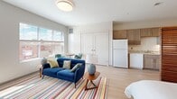 This 410 square foot studio apartment in Boston offers a thoughtfully designed living space that maximizes efficiency and style. The open-concept layout seamlessly integrates the living, sleeping, and kitchen areas, creating a sense of spaciousness within the compact footprint. Large windows flood the space with natural light, enhancing the bright and airy atmosphere.

The main living area features a comfortable blue sofa, complemented by a colorful striped rug that adds a playful touch to the neutral palette. A sleek kitchenette with light wood cabinetry and modern appliances occupies one wall, providing all essential cooking amenities without overwhelming the space.

The sleeping area is cleverly separated from the main living space by a stylish wooden slatted partition, offering a degree of privacy while maintaining the open feel. The bed is flanked by contemporary furnishings, including a wooden dresser and strategically placed lighting fixtures.

The bathroom, though compact, is well-appointed with clean lines and neutral tones. It includes a full-sized bathtub with shower, a modern vanity, and ample storage space. The large floor tiles contribute to a sense of spaciousness.

Throughout the apartment, the use of light wood flooring, white walls, and carefully chosen furniture pieces creates a cohesive and inviting environment. This studio efficiently combines functionality and contemporary design, making it an ideal urban dwelling for those seeking a minimalist yet comfortable lifestyle in the heart of Boston.