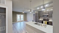 This well-designed single-floor residence offers a clean, contemporary aesthetic with a cohesive neutral color palette and light wood-style luxury vinyl flooring carried throughout every room. The open-concept layout connects the kitchen and living area seamlessly, creating an inviting and functional shared space. The kitchen is a standout feature, equipped with dark gray cabinetry, white countertops, stainless steel appliances including a refrigerator, electric range, and built-in microwave, as well as a peninsula with a double stainless steel sink and stylish pendant lighting overhead. A ceiling fan with integrated lighting anchors the living area, which benefits from natural light through French doors that open to the exterior. The two bedrooms are comfortably sized, each featuring windows that bring in natural light and ceiling fans for added comfort. The primary bathroom includes a vanity with a white countertop, open shelving, and a walk-in shower area, while the secondary bathroom is fitted with a full bathtub and shower combination. Track lighting and recessed fixtures provide well-distributed illumination throughout. The entry foyer offers a clean transition into the space, with the kitchen peninsula visible upon entry, reinforcing the open and airy character of the floor plan.