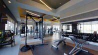 This fitness studio is a thoughtfully designed, single-floor facility that combines functionality with upscale aesthetics. The open floor plan provides generous space for a wide variety of workout activities, accommodating both strength training and functional fitness routines. The ceiling features a striking coffered design with bold yellow accent panels and integrated linear LED lighting, creating a bright, energizing atmosphere throughout the space. Recessed lighting further enhances visibility across all workout zones.

The studio is outfitted with an impressive selection of professional-grade equipment, including a cable machine, power rack, adjustable weight bench, battle ropes, and a full dumbbell rack arranged along one wall for easy access. Large windows allow natural light to fill the space, contributing to an open and inviting environment. Full-length mirrors are strategically positioned to expand the sense of space and assist users with form and technique.

The flooring combines rubberized workout matting with smooth transitional surfaces, providing both durability and comfort underfoot. The overall ambiance is sleek and modern, with a neutral color palette accented by metallic and warm tones that lend a polished, high-end feel to the studio.