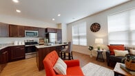 This single-floor residence at 2001 Traceway Dr in Fitchburg, Wisconsin offers a thoughtfully designed open-concept layout that seamlessly connects the living and kitchen areas. The kitchen is a standout feature, showcasing rich dark wood cabinetry, granite countertops, stainless steel appliances including a refrigerator, electric range, and built-in microwave, all set atop warm hardwood-style flooring. A central island with bar seating provides a casual dining option and flows naturally into the adjacent living space, which is bathed in natural light from large windows with horizontal blinds. The living room offers a comfortable, welcoming atmosphere with neutral walls and continued hardwood-style flooring throughout. The space includes two bedrooms, each carpeted and featuring windows that allow ample natural light. Both rooms offer a calm and restful ambiance with clean, simple finishes. The bathroom is designed with accessibility in mind, featuring grab bars, a roll-in shower, granite-topped vanity with dark wood cabinetry, and matching hardwood-style flooring. The overall design balances modern finishes with functional, accessible features, creating a bright and cohesive living environment.