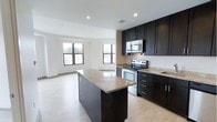 This single-floor 2-bedroom, 2-bathroom residence offers a thoughtfully designed open-concept layout that seamlessly connects the kitchen and living areas. The kitchen is a standout feature, boasting rich dark cabinetry that contrasts elegantly with light granite countertops. A center island provides additional workspace and doubles as a casual gathering spot. Stainless steel appliances, including a range and over-the-range microwave, complete the modern culinary space. Light hardwood-style flooring flows throughout, lending warmth and continuity to the interior. The open living area is bathed in natural light, courtesy of multiple large windows that frame views of the surrounding greenery. Recessed lighting throughout the space ensures a bright and welcoming ambiance at any time of day. The clean white walls and neutral palette create a versatile backdrop well-suited to a variety of interior styles. Overall, the residence strikes a balance between contemporary design and everyday functionality, offering a comfortable and stylish living environment across its two bedrooms and two bathrooms.