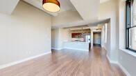 Located in the heart of downtown Albany at 90 State Street, this well-appointed 2-bedroom, 2-bathroom residence offers a thoughtfully designed open-concept layout across a single floor. Wide-plank hardwood flooring flows seamlessly throughout, connecting each living space with warmth and continuity.

The combined kitchen and living area serves as the centerpiece of the home. The kitchen features rich wood cabinetry, white subway tile backsplash, stainless steel appliances including a gas range and refrigerator, and a generous island with a light quartz countertop and integrated sink — ideal for both meal preparation and casual dining. Pendant lighting and a track light system add a modern, industrial touch overhead.

The spacious living room benefits from large arched windows that frame striking views of Albany's historic downtown skyline, flooding the space with natural light. A bright, light-filled hallway connects the living areas to the private quarters, leading to two well-sized bedrooms, each with hardwood floors and large windows offering city and landscape views.

The primary bedroom is generously proportioned, with dual windows inviting abundant sunlight. The bathrooms are finished with elegant details, including a walk-in glass-enclosed shower with white subway tile, mosaic tile flooring, and marble-look tile — conveying a clean, upscale aesthetic throughout.