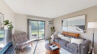 Located in Kentwood, Michigan, this one-bedroom, one-bathroom unit offers a well-designed single-floor layout that maximizes every inch of its cozy footprint. The open-concept living room and kitchen area serves as the heart of the home, bathed in natural light streaming through large sliding glass doors that open to a serene outdoor view of lush greenery and a nearby waterway. The living room offers ample space for comfortable seating and entertainment. The kitchen is a functional galley-style space featuring granite-look countertops, white shaker cabinetry, stainless steel appliances including a dishwasher, electric range, and refrigerator, complemented by wood-look flooring. A breakfast bar with seating connects the kitchen seamlessly to the living area, enhancing the open feel. The bedroom is a calm retreat with plush carpeting, a large window with drape treatments allowing natural light, and generous wall space for storage and décor. The bathroom is clean and straightforward, featuring a full shower-tub combination with neutral finishes. A hallway and entrance area complete the layout, providing a smooth flow throughout the unit. Neutral tones and clean lines give this home a bright, welcoming ambiance throughout.