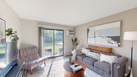 Located in Kentwood, Michigan, this one-bedroom, one-bathroom unit offers a well-designed single-floor layout that maximizes every inch of its cozy footprint. The open-concept living room and kitchen area serves as the heart of the home, bathed in natural light streaming through large sliding glass doors that open to a serene outdoor view of lush greenery and a nearby waterway. The living room offers ample space for comfortable seating and entertainment. The kitchen is a functional galley-style space featuring granite-look countertops, white shaker cabinetry, stainless steel appliances including a dishwasher, electric range, and refrigerator, complemented by wood-look flooring. A breakfast bar with seating connects the kitchen seamlessly to the living area, enhancing the open feel. The bedroom is a calm retreat with plush carpeting, a large window with drape treatments allowing natural light, and generous wall space for storage and décor. The bathroom is clean and straightforward, featuring a full shower-tub combination with neutral finishes. A hallway and entrance area complete the layout, providing a smooth flow throughout the unit. Neutral tones and clean lines give this home a bright, welcoming ambiance throughout.