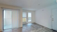 This single-floor space offers a clean, modern aesthetic defined by an open layout and an abundance of natural light. The main living area features smooth, light-toned hardwood-style flooring that runs throughout, complementing the crisp white walls and adding a sense of warmth and continuity to the space.

Large windows fitted with horizontal blinds allow generous daylight to fill the interior, while a set of sliding glass doors flanked by vertical blinds opens directly onto a private balcony, seamlessly connecting the indoor living area with the outdoors. The balcony provides an inviting extension of the living space, ideal for enjoying fresh air and outdoor views.

The textured ceiling adds subtle architectural character, while the overall neutral color palette creates a versatile backdrop well-suited to a variety of furnishing styles. The space is thoughtfully designed to feel open and airy, with a layout that maximizes both comfort and functionality. The combination of natural light, contemporary finishes, and outdoor access makes this a bright and welcoming environment throughout the day.