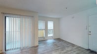 This single-floor space offers a clean, modern aesthetic defined by an open layout and an abundance of natural light. The main living area features smooth, light-toned hardwood-style flooring that runs throughout, complementing the crisp white walls and adding a sense of warmth and continuity to the space.

Large windows fitted with horizontal blinds allow generous daylight to fill the interior, while a set of sliding glass doors flanked by vertical blinds opens directly onto a private balcony, seamlessly connecting the indoor living area with the outdoors. The balcony provides an inviting extension of the living space, ideal for enjoying fresh air and outdoor views.

The textured ceiling adds subtle architectural character, while the overall neutral color palette creates a versatile backdrop well-suited to a variety of furnishing styles. The space is thoughtfully designed to feel open and airy, with a layout that maximizes both comfort and functionality. The combination of natural light, contemporary finishes, and outdoor access makes this a bright and welcoming environment throughout the day.