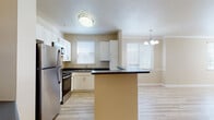 Located at 5050 Hacienda Dr in Dublin, CA, this single-floor residence offers a well-designed layout with a warm, neutral color palette throughout. The open-concept kitchen is a functional centerpiece, featuring white cabinetry, dark countertops, a central island, and a full suite of stainless steel appliances including a refrigerator, gas range, microwave, and dishwasher. Light wood-style flooring runs through the kitchen and connects seamlessly to the dining area, which is accented by an elegant chandelier and generous natural light from multiple windows. The spacious living room showcases crown molding, a ceiling fan, a wood-burning fireplace with a classic white surround, and a glass door leading to the outdoors. The bedroom is finished with plush carpeting and its own ceiling fan, offering a comfortable retreat. The bathroom includes a combination soaking tub and shower with tiled surround, white cabinetry, and dark countertops. Additional built-in shelving provides display and storage options throughout. A dedicated laundry area houses a full-size side-by-side washer and dryer, adding everyday convenience to this thoughtfully appointed single-level home.