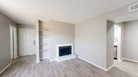 This single-floor, 2-bedroom, 2-bathroom residence offers a thoughtfully designed layout that maximizes functionality. The living room serves as the heart of the home, featuring light gray vinyl plank flooring, a textured ceiling, a white brick fireplace with built-in shelving alongside it, and a sliding glass door that invites natural light throughout the space. The galley-style kitchen is efficiently arranged with white shaker cabinetry, black hardware accents, light quartz countertops, a stainless steel sink, and stainless steel appliances including a refrigerator, range, and dishwasher. Both bedrooms are carpeted and include ceiling fans, ample closet space, and neutral gray walls. The primary bedroom features a walk-in closet with built-in shelving. Three closets in total provide generous storage throughout. The two bathrooms are cleanly finished — one features a full tub-shower combo with white tile surround, while the other offers a vanity with quartz countertop and modern black hardware accents. An in-unit laundry area adds everyday convenience. The consistent neutral color palette and updated finishes throughout lend the space a clean, move-in-ready aesthetic.