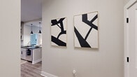This single-floor residence offers a cohesive, modern aesthetic with neutral tones, wood-look flooring, and carefully curated design details throughout. The open-concept living area features recessed lighting, large windows that invite natural light, and direct sightlines into the kitchen, creating a connected and airy feel. The kitchen is a standout, showcasing taupe shaker-style cabinetry reaching to the ceiling, dark granite countertops, stainless steel appliances, a built-in wine rack, and a peninsula with bar seating illuminated by industrial-style pendant lights. The primary bedroom is a comfortable retreat with plush carpeting, natural light from a large window, and access to a well-appointed en suite bath featuring a dual-sink white vanity with dark hardware, framed mirrors, and a glass-enclosed soaking tub with large-format tile surround. A walk-in closet with built-in shelving and hanging rods serves the primary suite. The second bedroom is equally inviting, with soft carpet and a calm, neutral palette. The second bathroom offers a tiled tub-shower combo, a dark-countered vanity, and marble-look tile flooring. Two hallways and additional closets provide excellent storage and easy circulation throughout the home.